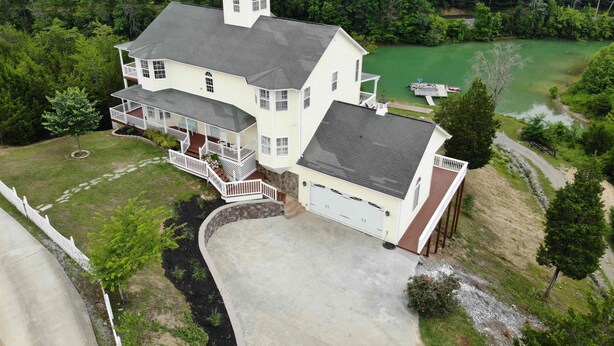 A large, two-story house with a garage, a covered porch, and a small tower. It is surrounded by a well-maintained lawn and a body of water. - Douglas Lake Waterfront Estate (Sevierville)