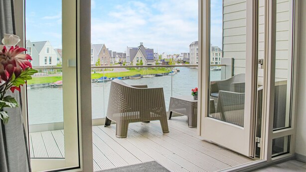Ein Balkon mit Korbmöbeln, Blick auf einen Fluss und Gebäude im Hintergrund.