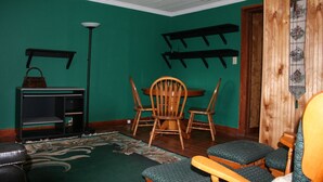 Een kamer met blauwgroene wanden, een houten plafond, een eettafel met stoelen, een zwarte entertainmentkast en een houten wanddecoratie.