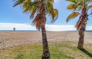 A beach with two palm trees and a lifeguard tower in the distance. - Villa Natalia (Benajarafe)