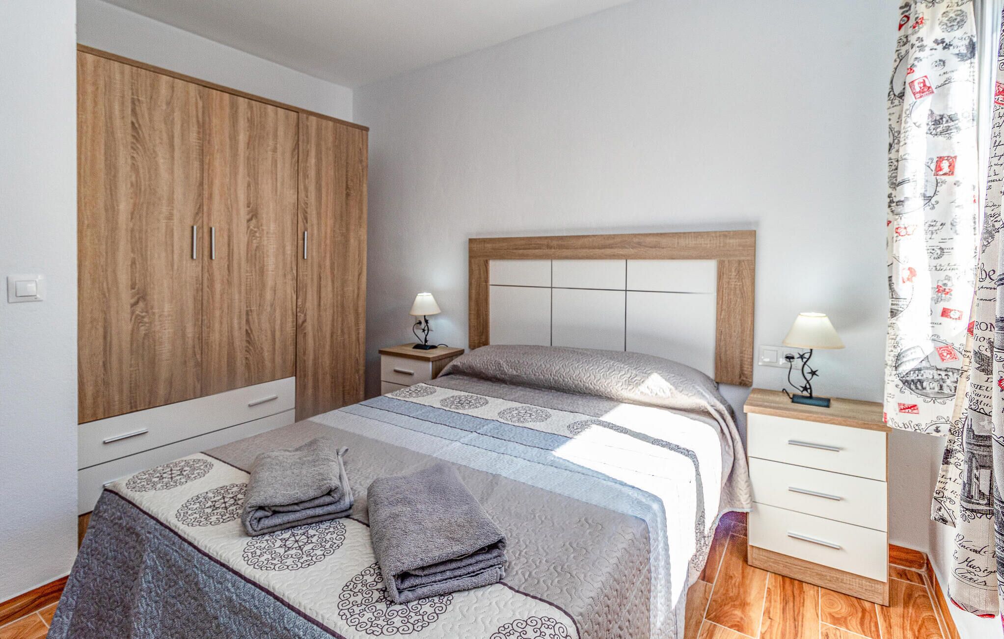 Un dormitorio con cama, mesitas de noche, armario y cortina.