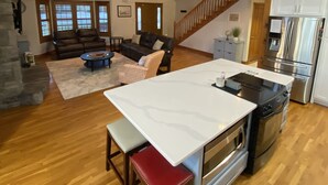 A spacious living area with a high ceiling, wooden beams, a stone fireplace, a dining area with a kitchen island, and a staircase leading to an upper level. - Lake house with boat ramp access across the street & tons of boat parking space. (Monticello)