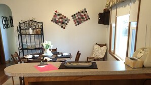 Una cucina con isola centrale, due sgabelli, un tavolo da pranzo con sedie, un elemento decorativo a parete e una finestra con tende.