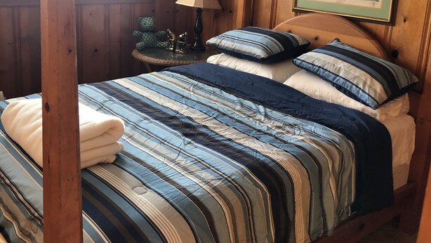 Una camera da letto con un letto a baldacchino in legno, un comodino con una lampada, un quadro appeso alla parete e una finestra con persiane.