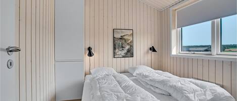 A bedroom with a bed, a wardrobe, a window with a view, and a wall-mounted lamp.