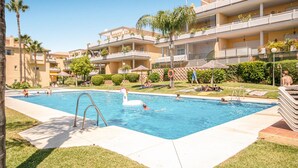 A swimming pool surrounded by a well-maintained lawn and palm trees, with a multi-story building in the background. - 2 bedroom awesome apartment in Marbella (Marbella)