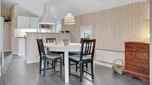 A modern kitchen with a central island, wooden walls, and a dining area with two chairs and a table.