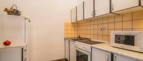A compact kitchen with white cabinets, a built-in oven, a microwave, and a sink.