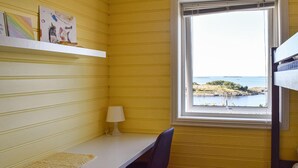Quarto com escrivaninha, cadeira e janela com vista para a água e terra.