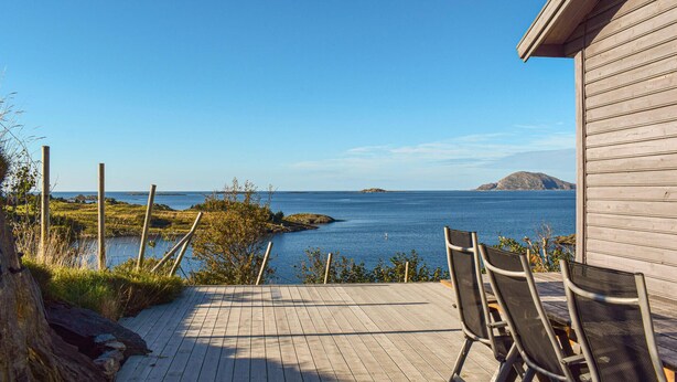 Um deck de madeira com cadeiras oferece vista para um mar calmo, uma ilha distante e um céu claro.