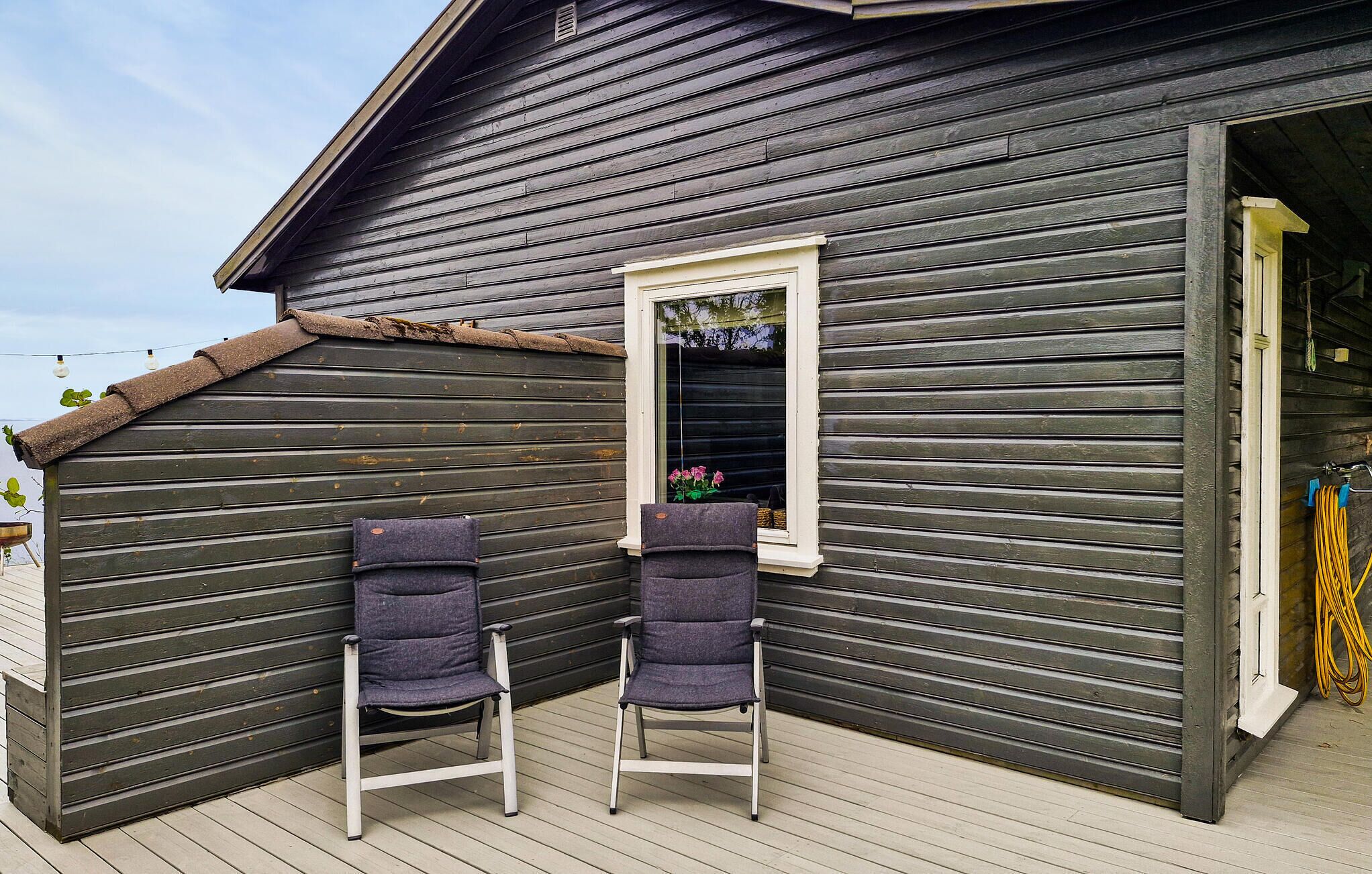A wooden exterior with a window and two chairs outside.