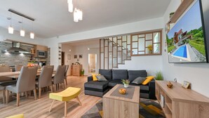 En moderne stue med sofa, sofabord og stole. Der er en trappe til et andet niveau, og et køkken er synligt i baggrunden.