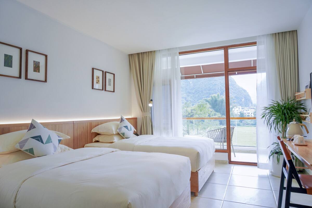 A hotel room with two beds, a balcony with a view of the mountains, and a dining area with a table and chairs.