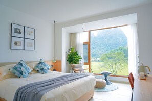 A bedroom with a large bed, a bedside table, a chair, a window with a view of a mountain, and a plant. - Yangshuo Enjoy Field Resort (Guilin)