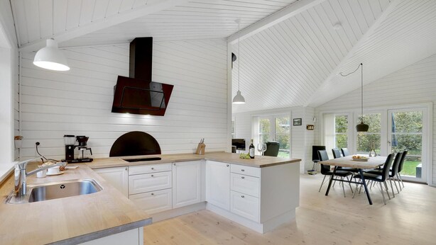 A spacious kitchen with white cabinetry, a central island, and a dining area with a table and chairs. - 3 bedroom beautiful home in Gilleleje (Gilleleje)