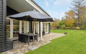 Eine Terrasse mit Tisch und Stühlen, ein überdachter Sitzbereich und ein Rasenstück.