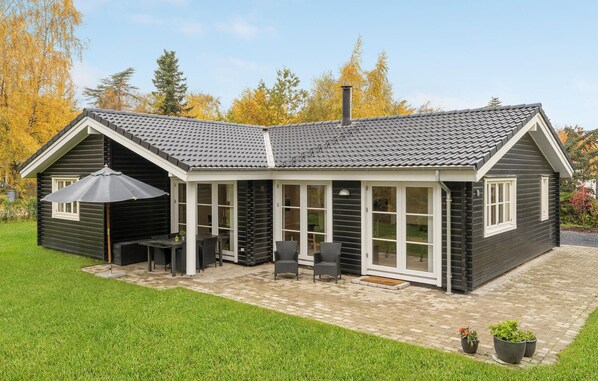 Ein zweistöckiges Haus mit dunkler Fassade, einem Ziegeldach und einer überdachten Terrasse mit Gartenmöbeln.