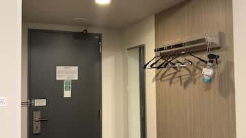 Un pasillo con una puerta negra, un equipo de aire acondicionado en la pared y un perchero con un pulverizador.