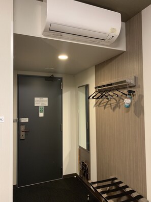 A hallway with a black door, an air conditioning unit mounted on the wall, and a coat rack with a spray bottle.