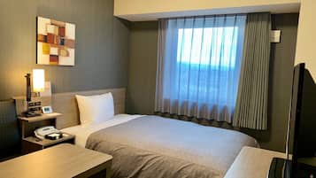 Ein Hotelzimmer mit Bett, Schreibtisch, Telefon, Fernseher und einem Fenster mit Vorhängen.