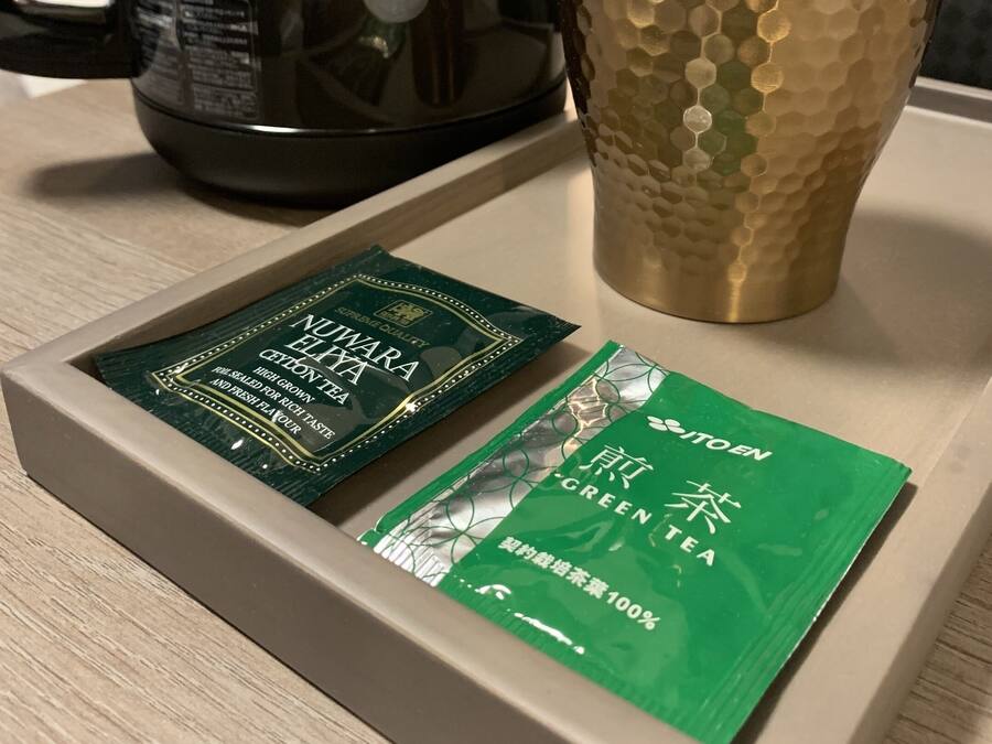 Una bandeja con una cafetera negra, una taza con textura y dos paquetes de té verde.