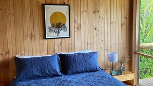 A wooden-paneled room with a bed, a framed picture, and a nightstand with a lamp and vases. - Bush Farm overlooking quiet valley  (Clarence Town)