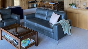 A cozy cabin interior with a wooden ceiling, a dining area, and a living room with leather sofas and a coffee table. - Bush Farm overlooking quiet valley  (Clarence Town)