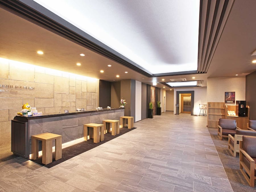 A hotel reception area with a reception desk, wooden stools, seating area, and a modern interior design.