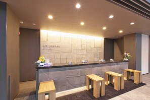 A reception area with a stone wall, a reception desk, and wooden stools. - Hotel Route Inn Kusatsuritto Rittointer -Ritto inter Kokudo 1gou (Ritto)
