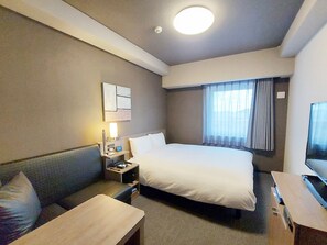 A hotel room with a bed, a desk, a chair, a nightstand, a TV, and a window with curtains.