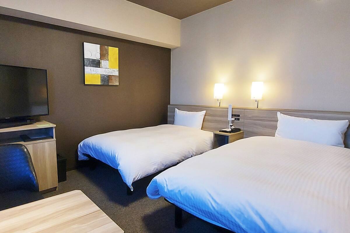 A hotel room with two beds, a TV, and a desk.