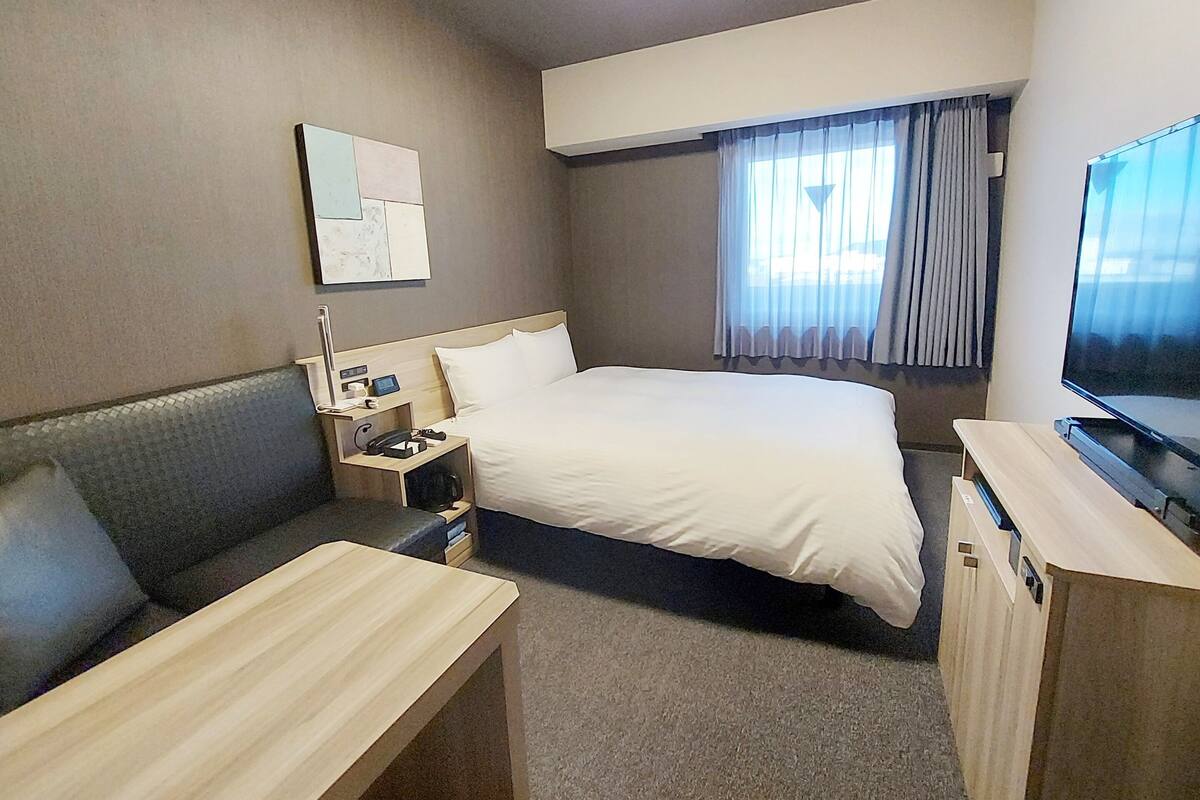 A hotel room with a bed, a desk, a chair, a TV, and a window with curtains.