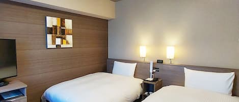 Una camera d'albergo con due letti singoli, una scrivania con una sedia, una televisione a schermo piatto e un condizionatore d'aria a parete.