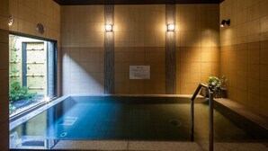 A hot tub with a view of a garden, surrounded by tiled walls and two wall-mounted lights. - Hotel Route Inn Tsuyama Ekimae (Tsuyama)