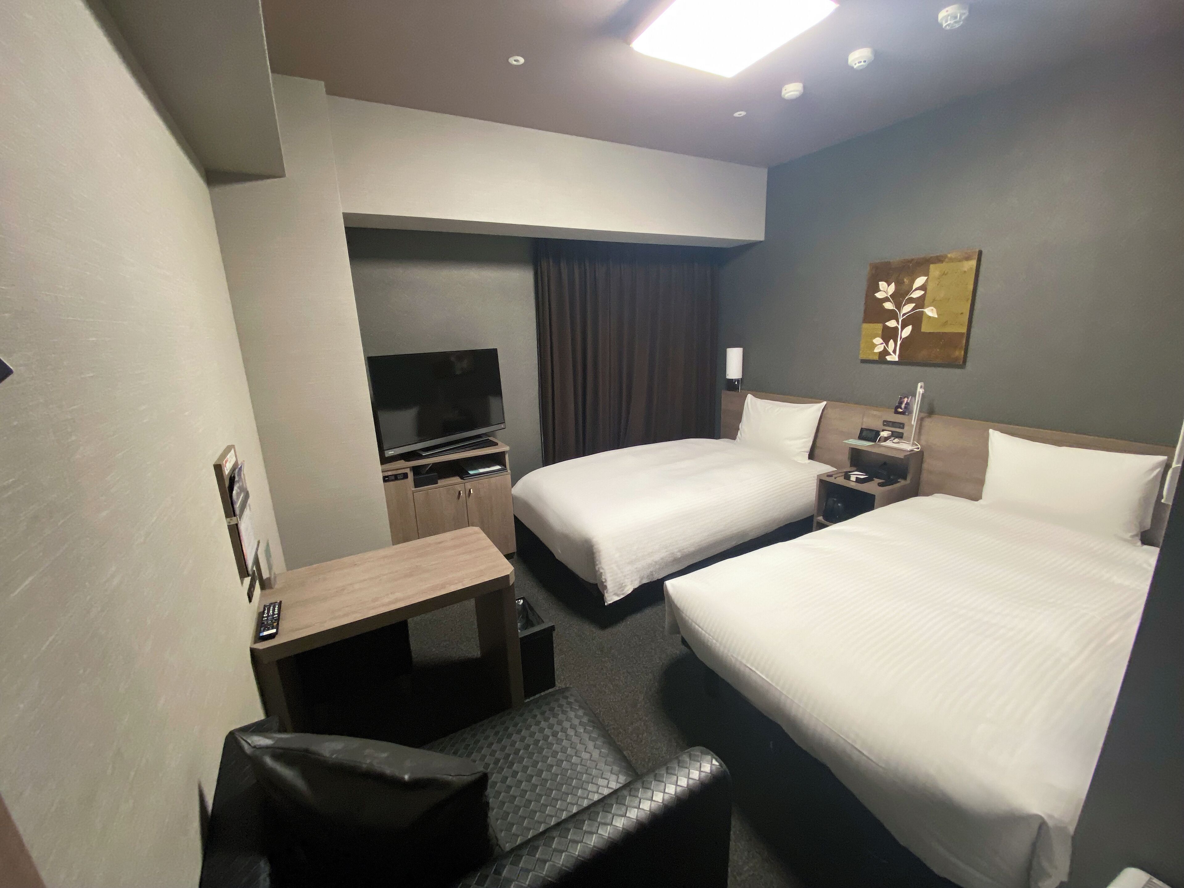 Una habitación de hotel con dos camas, un escritorio, un televisor y una pequeña mesa con una silla.