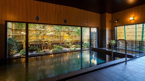 A modern indoor pool area with wooden paneling, large windows, and a view of a bamboo garden. - Hotel Route Inn Tsuyama Ekimae (Tsuyama)