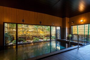 A modern indoor pool area with wooden paneling, large windows, and a view of a bamboo garden. - Hotel Route Inn Tsuyama Ekimae (Tsuyama)