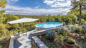 A backyard with a swimming pool, a covered patio with a table and chairs, and a large umbrella. - Nice apartment in Kastav (Kastav)