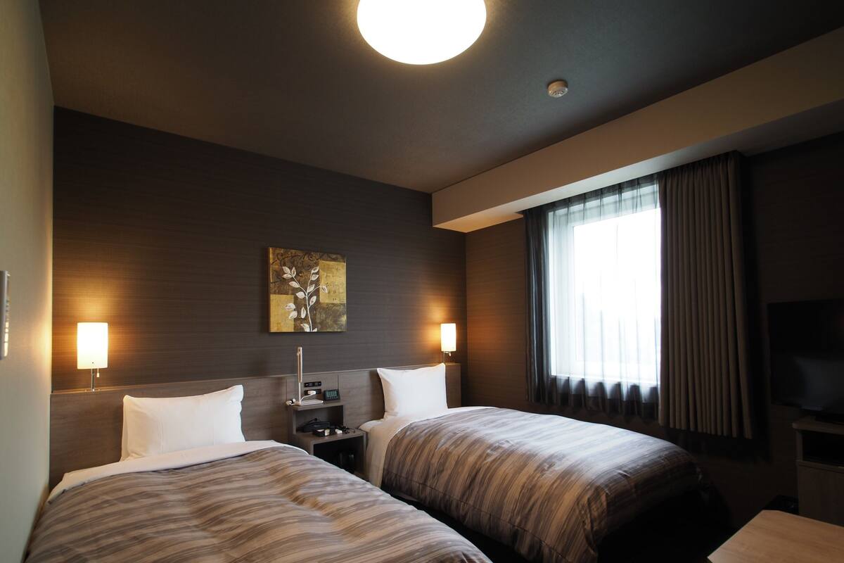 A hotel room with two beds, a flat-screen TV, a bedside table, a lamp, and a painting on the wall.