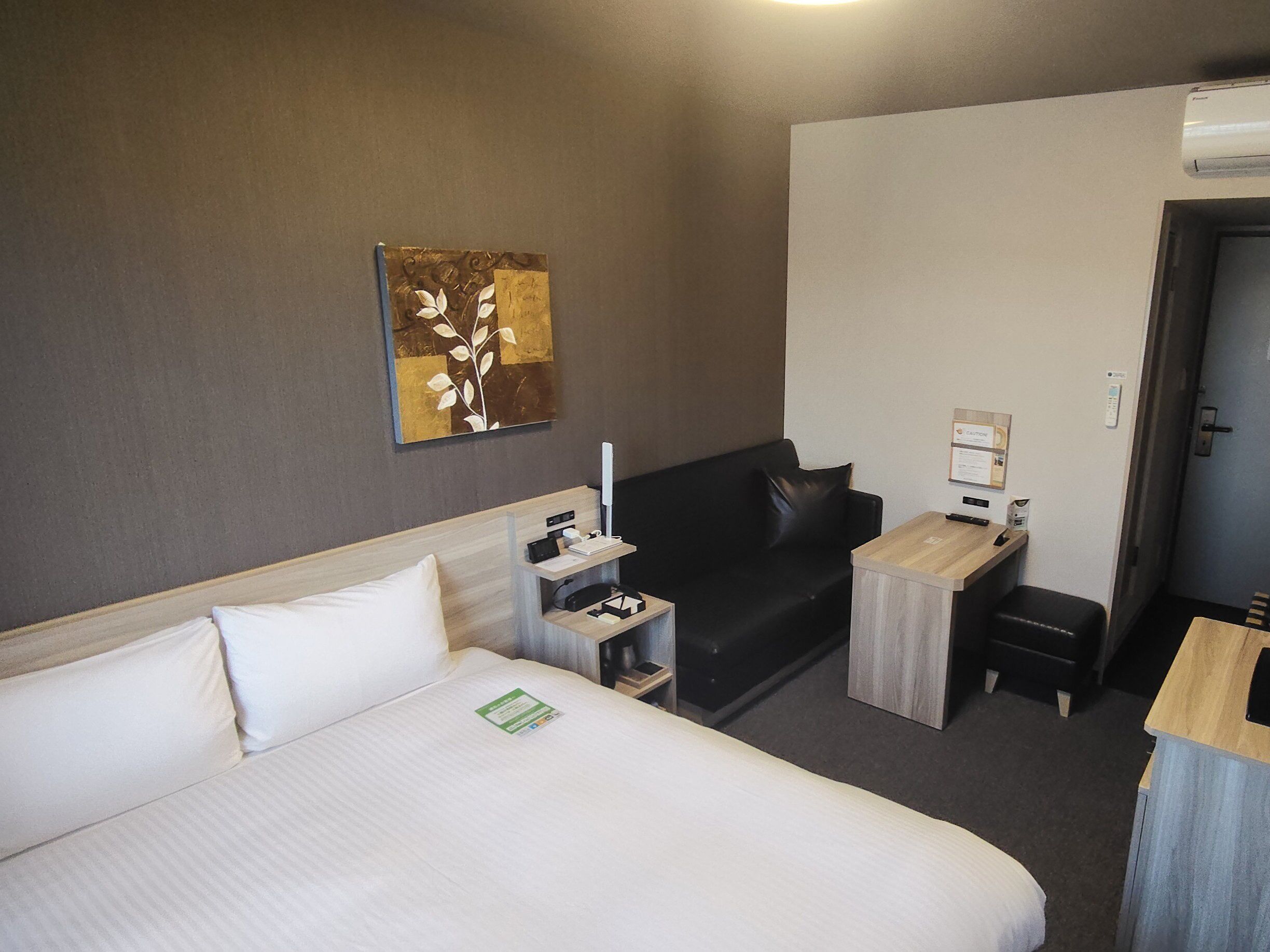 A hotel room with a large bed, a desk, a sofa, and a wall-mounted artwork.