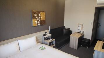 A hotel room with a large bed, a desk, a sofa, and a wall-mounted artwork.