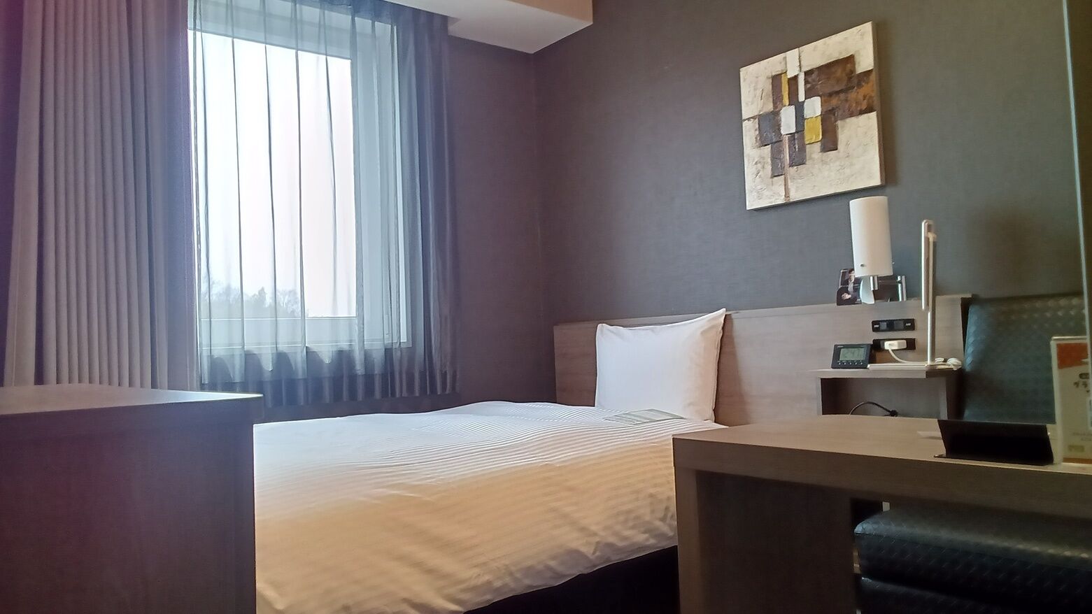 Une chambre d’hôtel comprenant un lit, un bureau, une chaise, une table de chevet, une lampe et une œuvre d’art accrochée au mur.