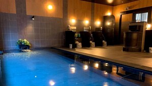 Una piscina con piso y paredes de azulejos, rodeada por un muelle de madera. Se observan varias bancas y una pequeña planta cerca de la piscina.