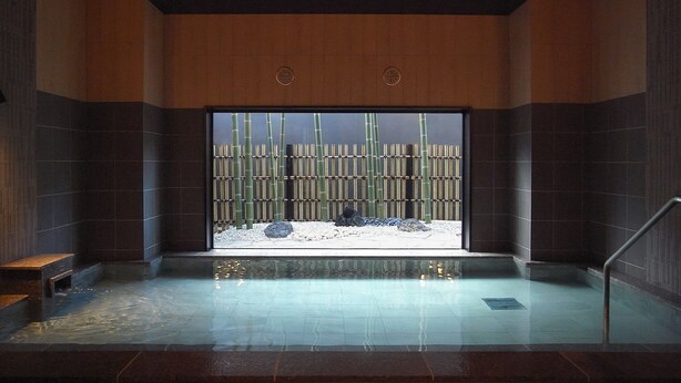 Un área de piscina interior moderna con vistas a bambú y rocas a través de un gran ventanal.