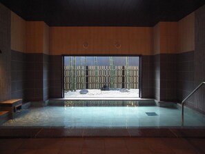 Zona d'una piscina interior moderna amb vista a bambú i roques a través d'un gran finestral.