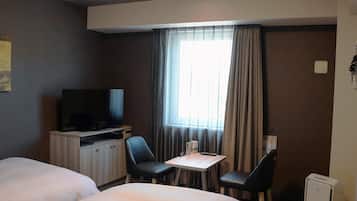 A hotel room with two beds, a TV, a small table with chairs, and a window with curtains.
