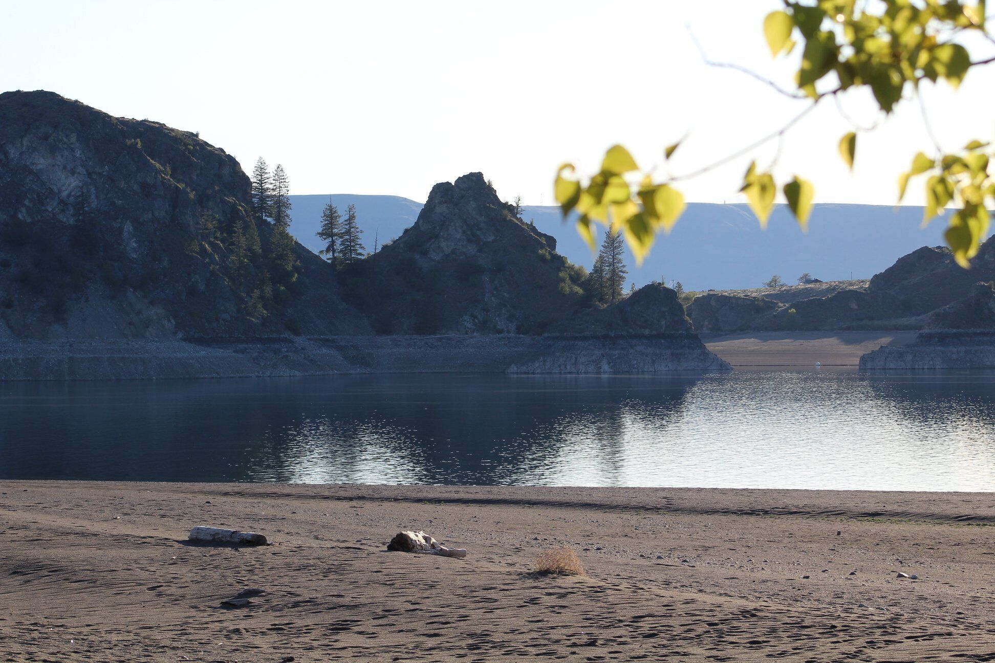 A natural landscape with a lake, rocky cliffs, and sparse vegetation.