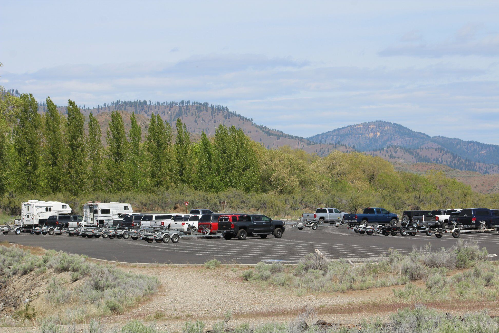 A parking lot with RVs and trucks, surrounded by trees and hills.
