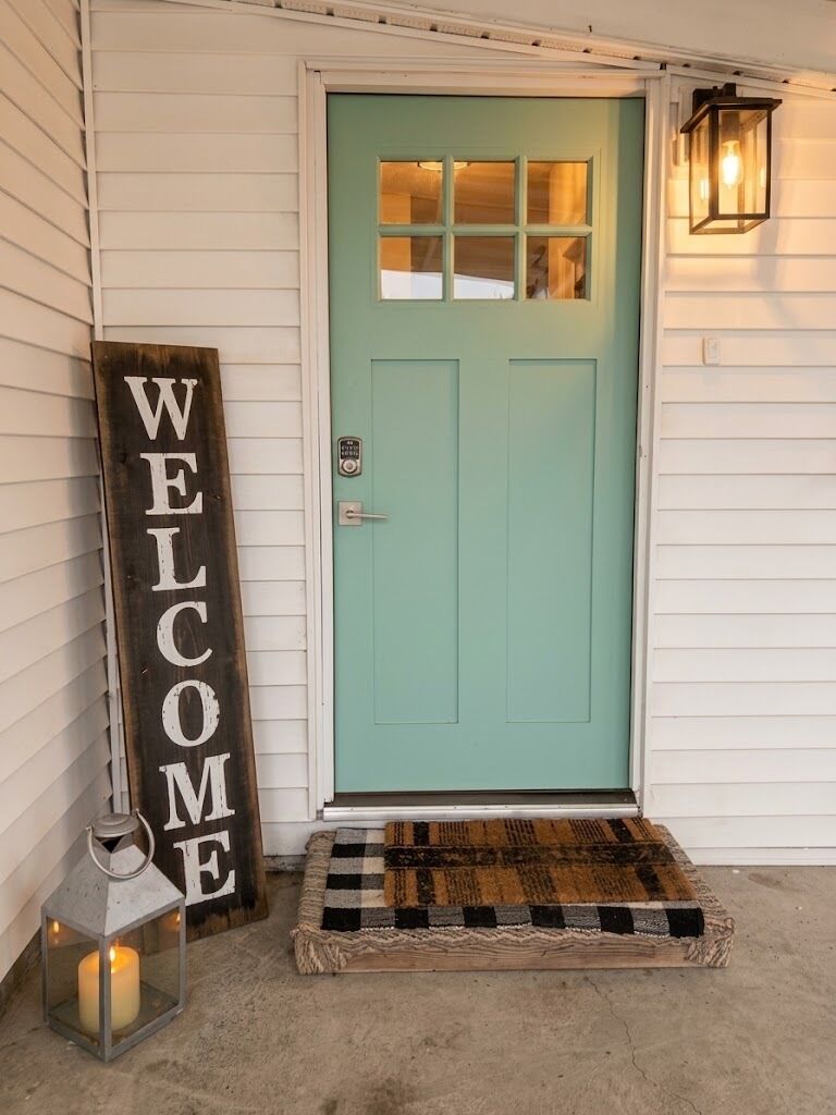 A teal door with a welcome sign, a lantern, and a checkered mat.