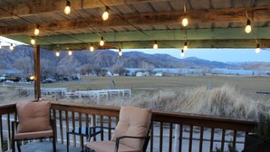 A covered outdoor seating area with two chairs and a table, overlooking a field and mountains. - Fishing Bungalow at Keller Ferry (Wilbur)
